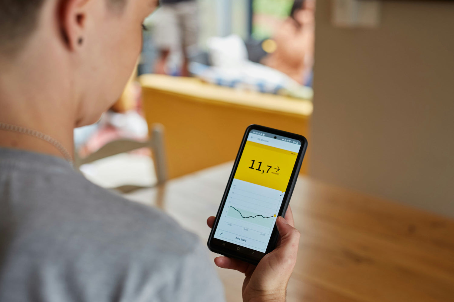 Person holding a smartphone with a screen displaying numbers and graphs representing the blood sugar data from their CGM.